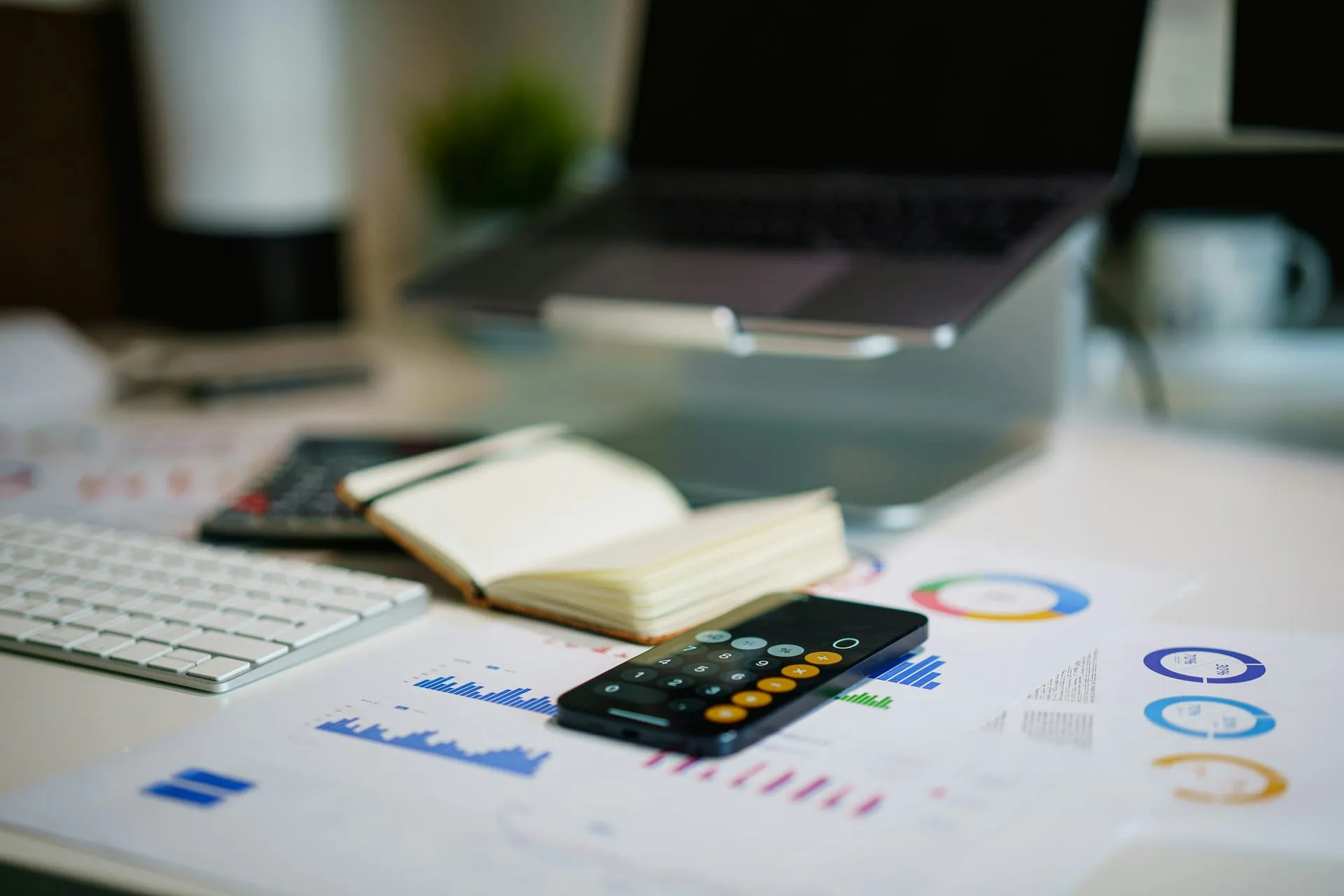 A desk with financial charts, a calculator, an open ledger and a laptop